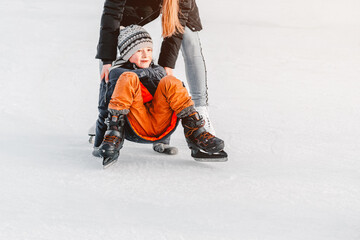 Soft,Selective focus.Mom with baby boy 6 years old, learn train, ride winter city rink, ice skating. The child gets up, fell on skates, kneels, play fun rest on weekend first steps child skates