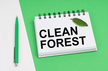 On a white-green background lies a pen, a leaf of a plant and a notepad with the inscription - Clean forest