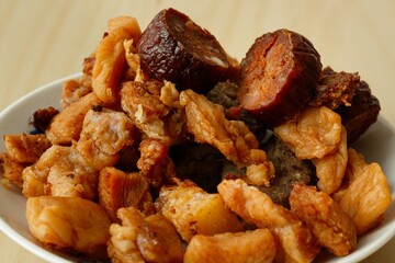 Close up of white porcelain plate full of crispy salty pork greaves on wooden desk with white background
