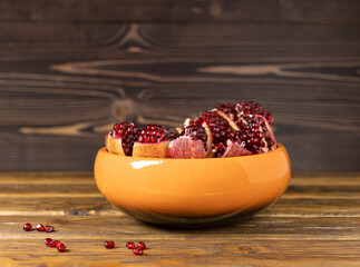 Sliced ripe pomegranate fruits lie in a deep ceramic bowl on a wooden table. Selective focus.