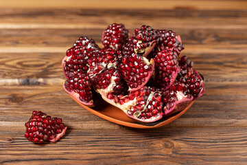 Slices of ripe pomegranate on a clay plate and a wooden table. Close-up, soft focus.