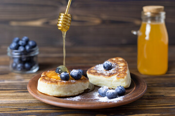 Pancakes, cottage cheese, lie on a plate with ripe blueberries and honey in a rustic style. Close-up. Selective focus.