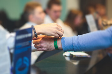 Process of checking in on a conference congress forum event, registration desk table, visitors and attendees receiving a name badge and entrance wristband bracelet and register electronic ticket,