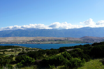 White clouds on the blue sky above green mountain and blue sea and green flora on the landscape in foreground