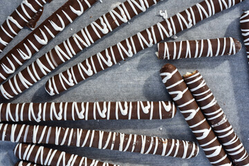 Milk chocolate coated pretzel sticks decorated with white chocolate drizzled stripes repeating pattern