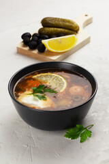 Traditional russian meat soup Solyanka in a black bowl and ingredients