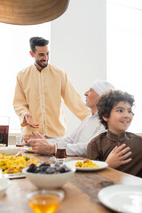 Smiling muslim man talking to mature father near tasty food at home.