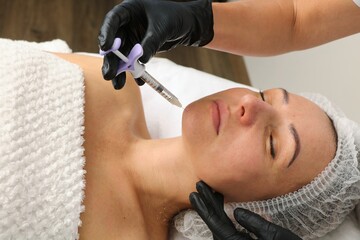 A beautician injects a facial rejuvenation injection into a middle-aged woman.