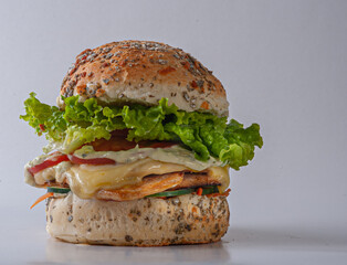 Chicken sandwich with melted cheese, mayonnaise, lettuce, tomato and pickles on hamburger bun