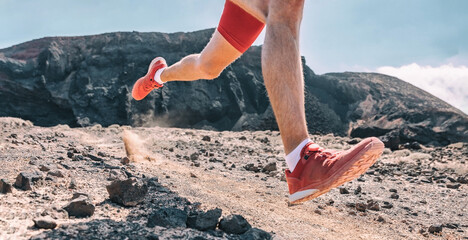 Trail running man on exercising racing fast on volanic trek path in mountain landscape. Closeup of athlete's foot and shoes jogging outdoors.
