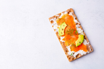 Sandwich with smoked salmon and cream cheese on thin multi seed crispbread, garnished with olives.