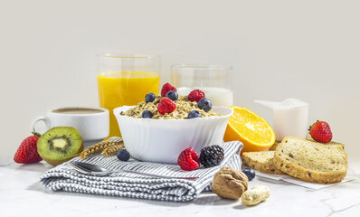 healthy breakfast of granola with blueberries, and raspberries in a white porcelain bowl, with fruit, nuts, milk, coffee, and wheat toast. front view