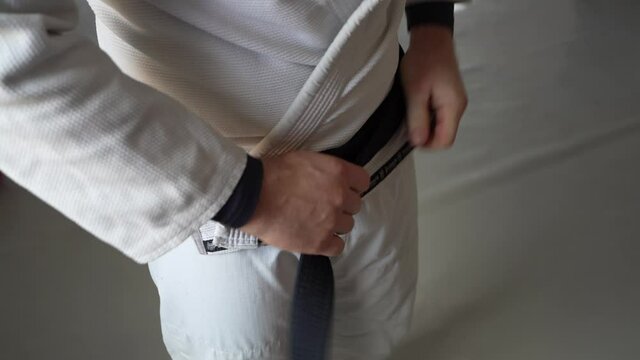 brazilian jiu jitsu bjj black belt male athlete holding belt tie around waist adjusting knot 
