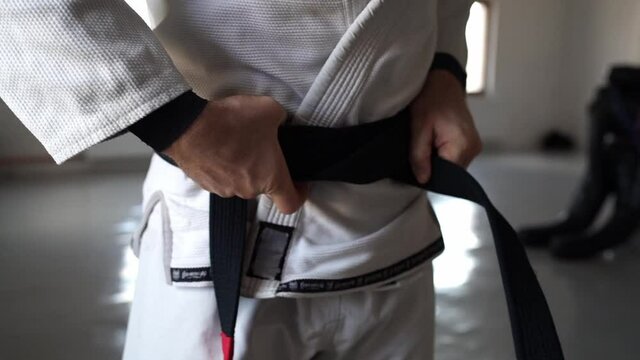 brazilian jiu jitsu bjj black belt male athlete holding belt tie around waist adjusting knot 