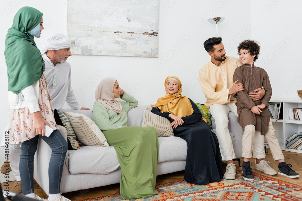 Wall mural young arabian man hugging son near multicultural muslim family at home.