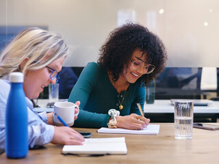 UK, London, Two smiling women writing in notebooks in modern office