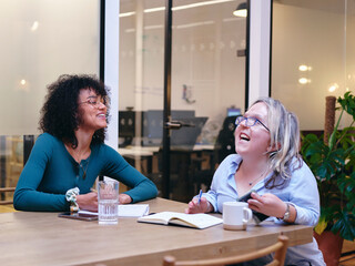UK, London, Two smiling women writing in notebooks in modern office - obrazy, fototapety, plakaty