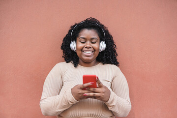 Happy african girl using mobile phone while listening music playlist with wireless headphone