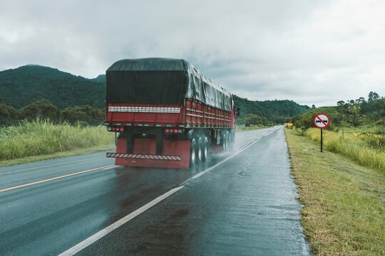 Cargo truck passing fast along the highway on a rainy day. In the background, the rainforest.