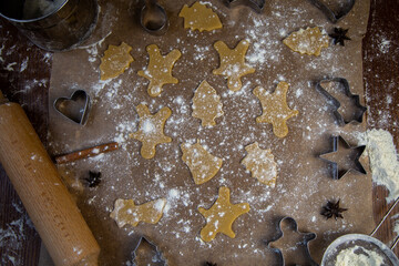 There are ready-made cookies of different shapes on the parchment, a rolling pin, cookie cutters and a sieve with flour are lying nearby, flour is scattered everywhere. High quality photo