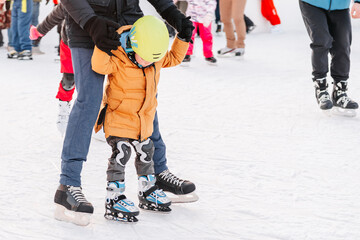 Soft,Selective focus.Funny moment fell on the ice skating rink. Activity, Adult, Child, Childhood, Daughter. Mom with baby boy 3-5 years old, learn train, ride winter city rink, ice skating. - obrazy, fototapety, plakaty