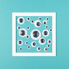 Sticker eyes in various sizes in a square frame on a pastel blue background. Supervision minimal background.