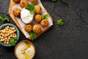 Traditional oriental chickpea deep fried falafel on a wooden board, tzatziki yoghurt sauce, hummus, fresh lime and green cilantro on black surface, copy space