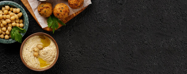 Traditional oriental chickpea deep fried falafel on a wooden board, tzatziki yoghurt sauce, hummus, fresh lime and green cilantro on black surface, copy space, banner