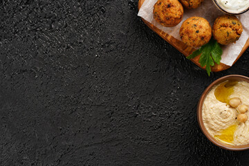 Traditional oriental chickpea deep fried falafel on a wooden board, tzatziki yoghurt sauce, hummus, fresh lime and green cilantro on black surface, copy space