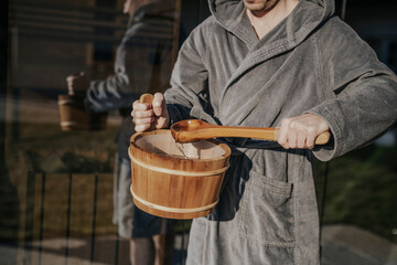 Mann mit Aufgussbottich vor der Sauna