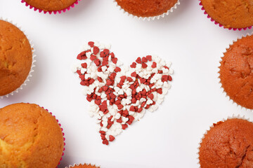 Red and white heart-shaped decoration for baking on white surface framed by muffins and cupcakes