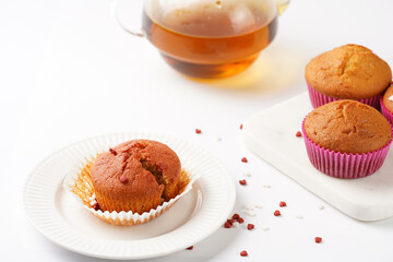 Several homemade white and pink muffins on marble board on white surface with heart-shaped red and white sugar decoration and tea-pot