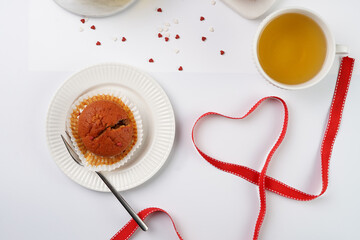 Several homemade white and pink muffins on marble board on white surface, red ribbon, heart-shaped red and white sugar decoration and tea-pot