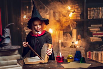 Little witches reads magic book while holds magic wand. Halloween party. Cosplay 