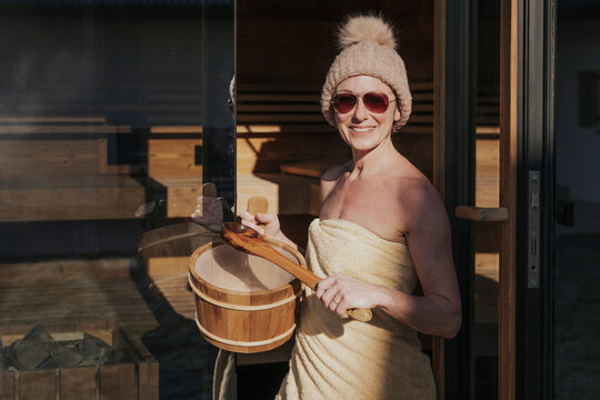 Frau mit Aufgussbottich vor der Sauna