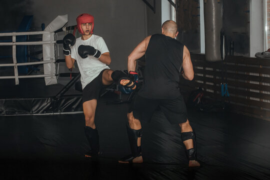 Two sportsmen boxers of different ages train in the classroom in the gym. They are practicing the Thai boxing technique in pairs