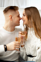 Fair-haired man and woman in white with glasses of champagne looking at each other while celebrating st valentines day