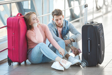 Couple sitting at the floor in airport. The flight delayed.