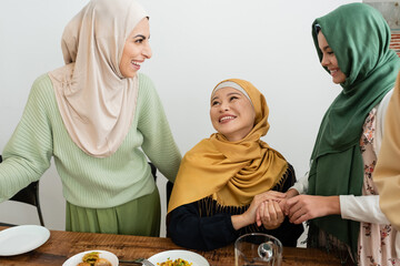 Smiling arabian woman looking at daughter and asian mom near food at home.