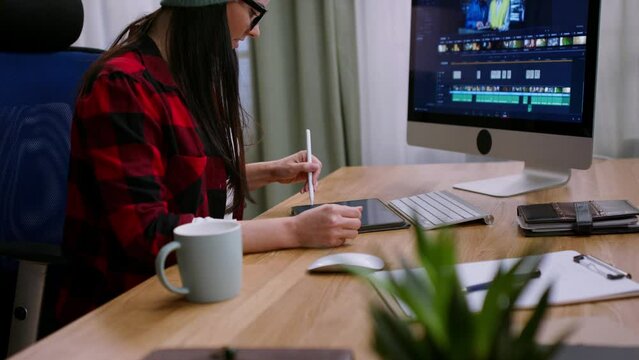 Female video editor works with footage on her personal computer indoors in creative office studio.