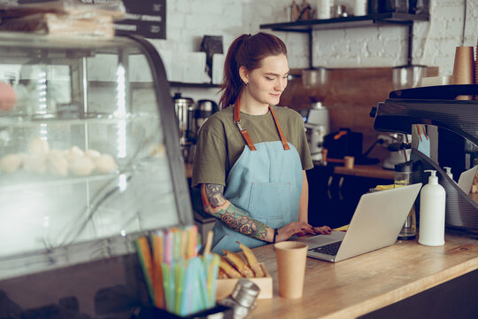 Young Woman Barista Using Laptop In Coffee Shop