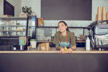 Joyful female barista standing behind counter in cafe