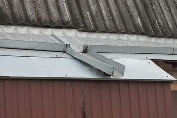 gray metal gutter on the roof of a private house over a brown iron wall on the street