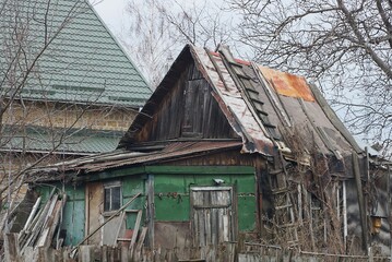 old rural green house with a gray roof on the street behind a fence