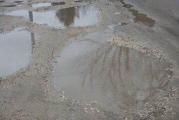many pits and puddles with dirty brown water on the road from gray earth on the street