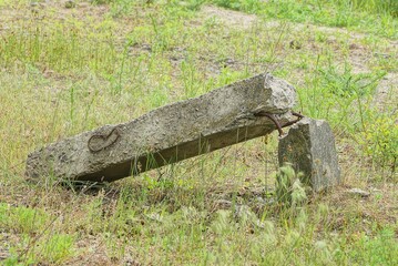one old gray broken concrete pillar lies in the green grass on the street