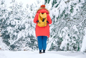 Woman in a red warm jacket and with a backpack on a background of snowy forest