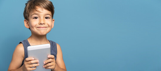 Front view of small caucasian boy four years old standing in front of blue background studio shot standing and using digital tablet looking to the camera happy smiling