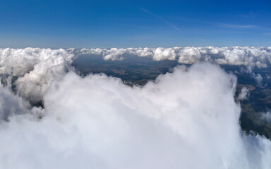 Obraz premium Aerial view from airplane window at high altitude of earth covered with puffy cumulus clouds forming before rainstorm