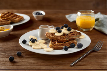 Oatmeal Belgian waffles topped with banana and blueberry on rustic wooden table